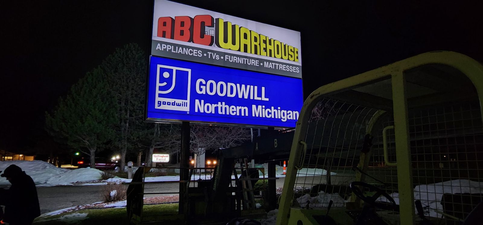 Lit pylon sign with ABC Warehouse and Goodwill Northern Michigan panels at night
