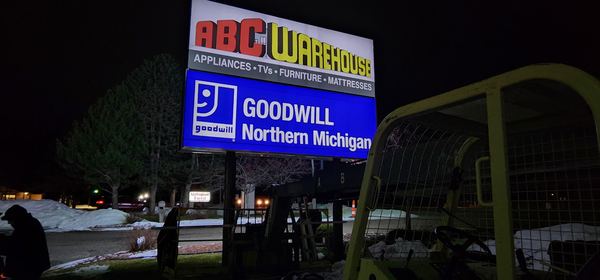 Lit pylon sign with ABC Warehouse and Goodwill Northern Michigan panels at night
