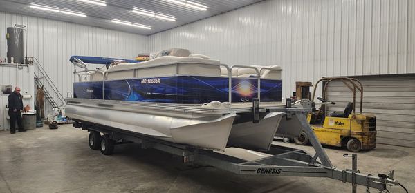 Pontoon boat on a trailer with blue printed wrap graphics, inside the shop
